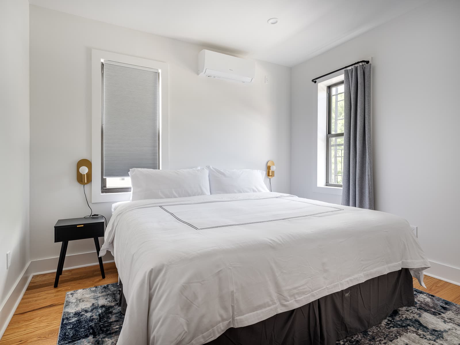 Bedroom with brass disc sconces, black nightstand and a blue abstract rug